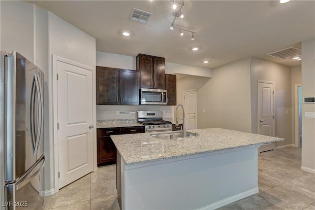 4441 Glossier Ave, North Las Vegas, NV 89084 - kitchen featuring stainless steel appliances, dark brown cabinetry, a center island with sink, light stone countertops, and light tile patterned floors