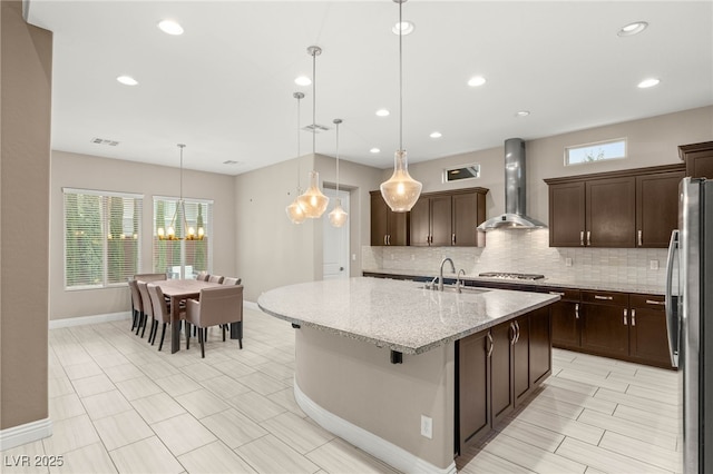 5676 Corona Vista St, Las Vegas, NV 89135 - kitchen featuring wall chimney exhaust hood, stainless steel appliances, a chandelier, tasteful backsplash, and dark brown cabinets