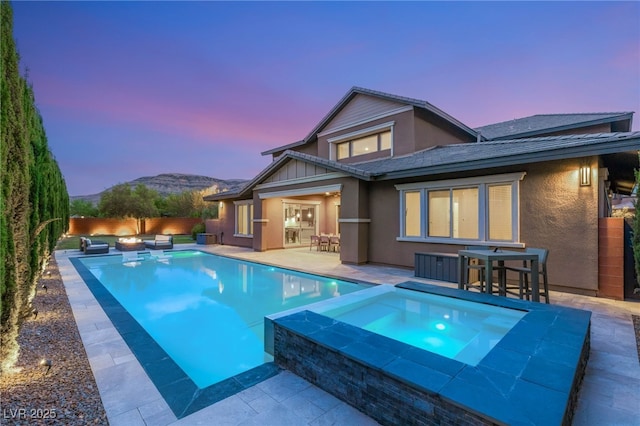 5676 Corona Vista St, Las Vegas, NV 89135 - back of property at dusk featuring an in-ground hot tub, a patio, stucco siding, an outdoor living space with a fire pit, and a mountain view