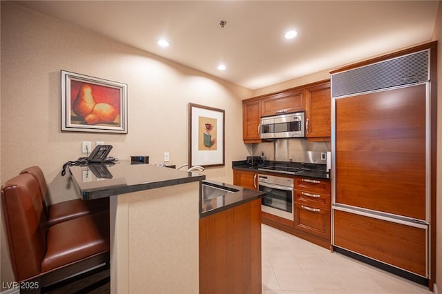 135 E Harmon Ave Unit 414, Las Vegas, NV 89109 - kitchen featuring stainless steel appliances, brown cabinetry, a peninsula, a kitchen bar, and dark countertops
