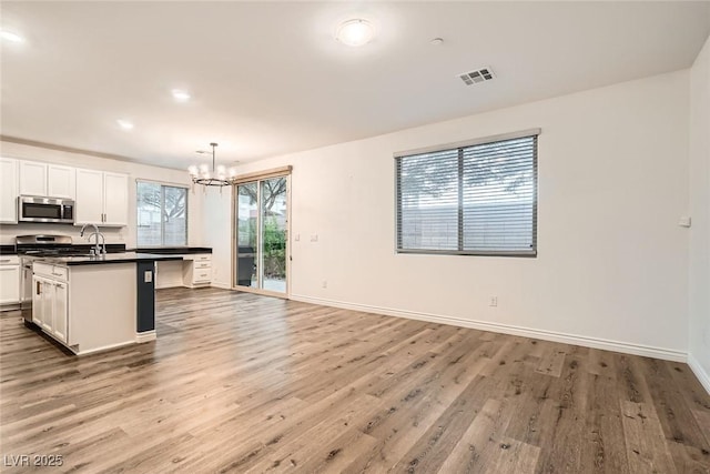 1009 Bluebell Brook St, Henderson, NV 89052 - kitchen featuring stainless steel appliances, dark countertops, a chandelier, wood finished floors, and a center island with sink
