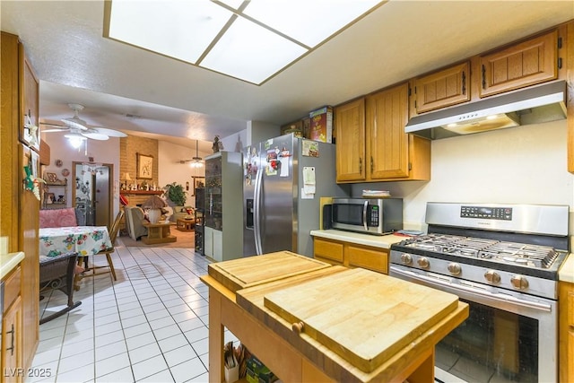 744 Milstead Ct, Las Vegas, NV 89110 - kitchen with stainless steel appliances, under cabinet range hood, light tile patterned floors, butcher block counters, and brown cabinetry