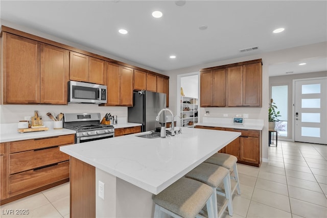 1309 Azure Jay Ave, North Las Vegas, NV 89084 - kitchen featuring stainless steel appliances, light tile patterned floors, recessed lighting, an island with sink, and brown cabinetry