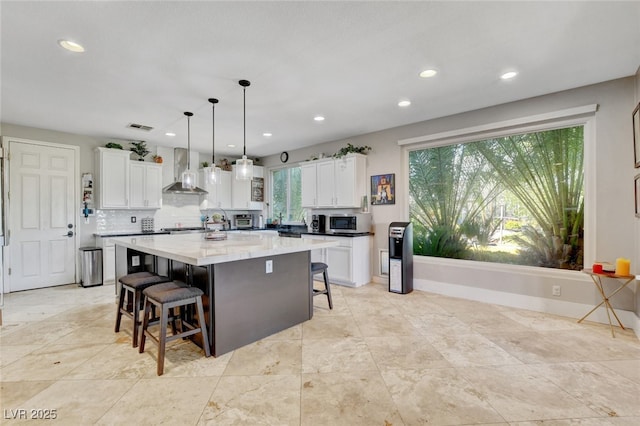 10960 Bethel Park Ct, Las Vegas, NV 89141 - kitchen featuring stainless steel microwave, wall chimney exhaust hood, a breakfast bar, white cabinetry, and recessed lighting