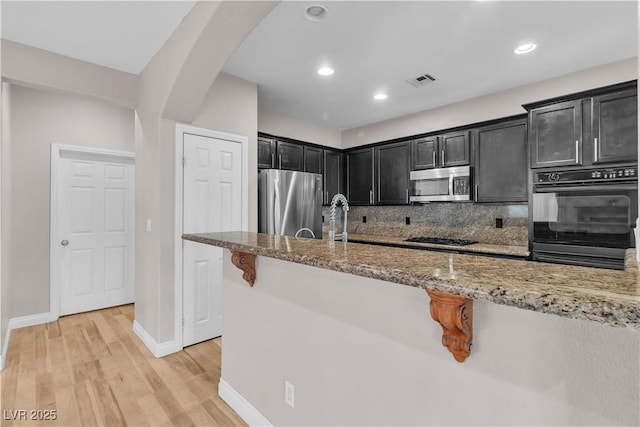 5001 Pounding Surf Ave, Las Vegas, NV 89131 - kitchen featuring stainless steel appliances, dark cabinetry, light stone countertops, light wood-style flooring, and arched walkways
