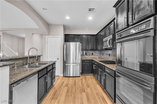 5001 Pounding Surf Ave, Las Vegas, NV 89131 - kitchen with stainless steel appliances, arched walkways, light wood-style floors, stone countertops, and backsplash