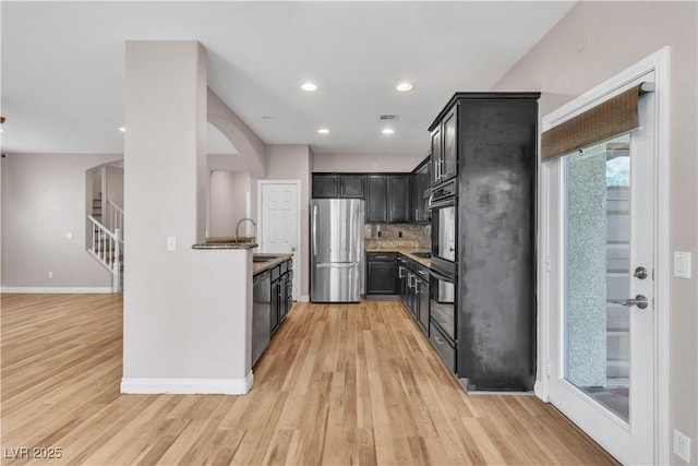 5001 Pounding Surf Ave, Las Vegas, NV 89131 - kitchen featuring stainless steel appliances, light wood finished floors, dark cabinetry, decorative backsplash, and arched walkways