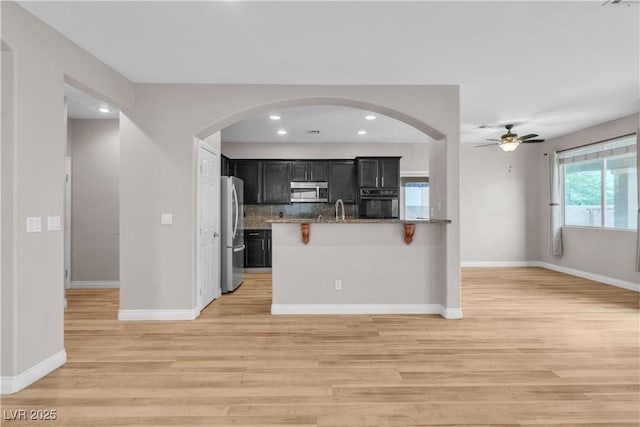 5001 Pounding Surf Ave, Las Vegas, NV 89131 - kitchen featuring stainless steel appliances, dark cabinetry, light wood-style flooring, open floor plan, and stone countertops