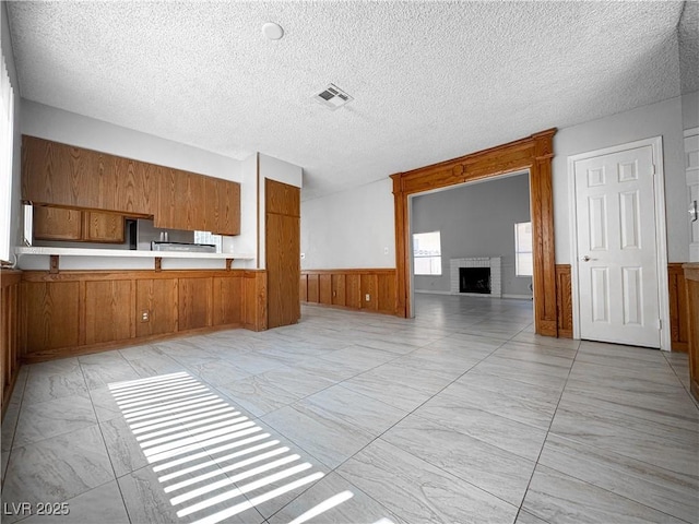 6437 Peachwood Rd, Las Vegas, NV 89108 - unfurnished living room with light marble finish flooring, a wainscoted wall, a brick fireplace, a textured ceiling, and wooden walls