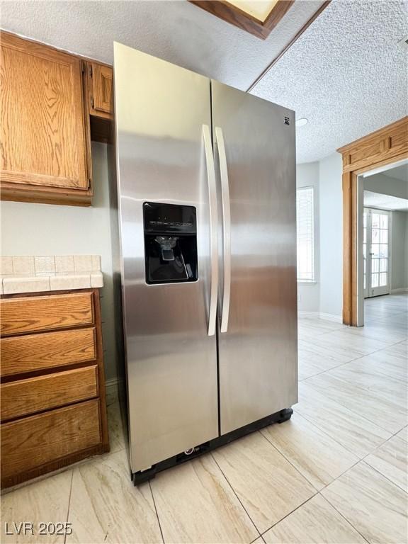 6437 Peachwood Rd, Las Vegas, NV 89108 - kitchen featuring stainless steel fridge, brown cabinetry, a textured ceiling, and tile countertops