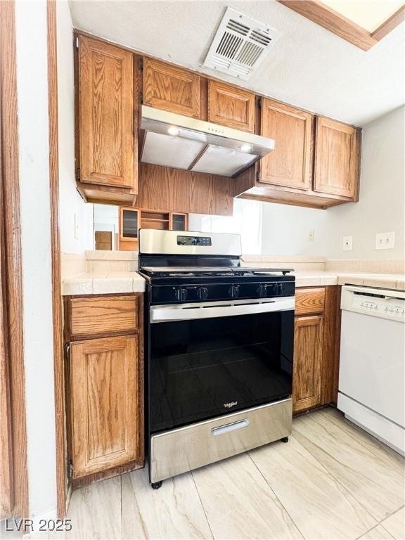 6437 Peachwood Rd, Las Vegas, NV 89108 - kitchen with stainless steel gas range oven, dishwasher, under cabinet range hood, and tile counters
