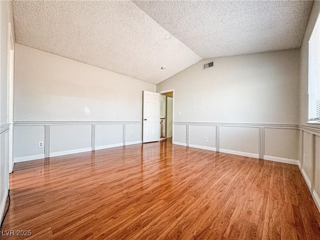6437 Peachwood Rd, Las Vegas, NV 89108 - empty room featuring a textured ceiling, wood finished floors, vaulted ceiling, a wainscoted wall, and a decorative wall