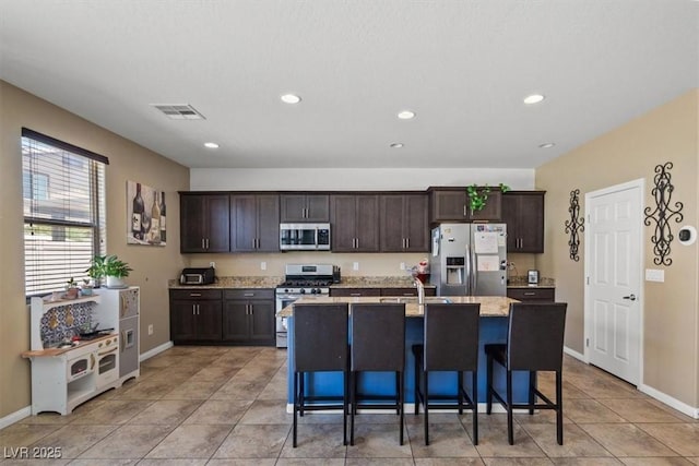5309 Golden Melody Ln, North Las Vegas, NV 89081 - kitchen featuring stainless steel appliances, dark brown cabinets, an island with sink, a kitchen bar, and light tile patterned floors