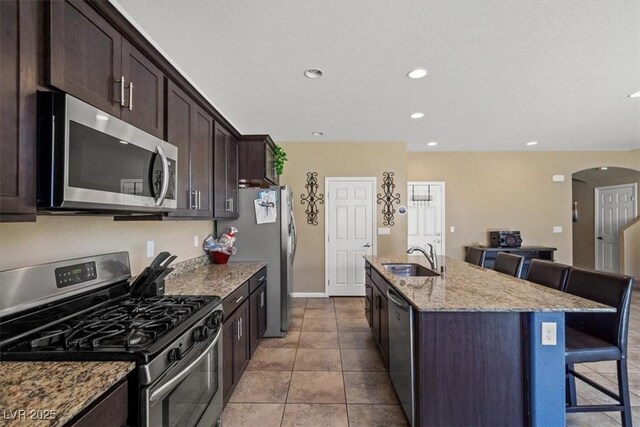 5309 Golden Melody Ln, North Las Vegas, NV 89081 - kitchen with appliances with stainless steel finishes, a kitchen bar, arched walkways, a kitchen island with sink, and light stone countertops
