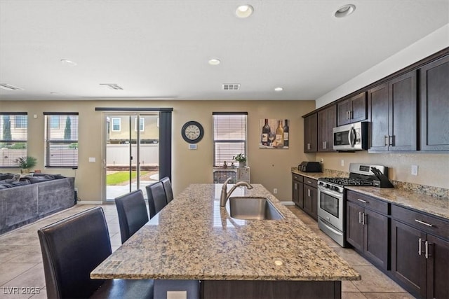 5309 Golden Melody Ln, North Las Vegas, NV 89081 - kitchen featuring appliances with stainless steel finishes, open floor plan, light tile patterned flooring, an island with sink, and light stone counters