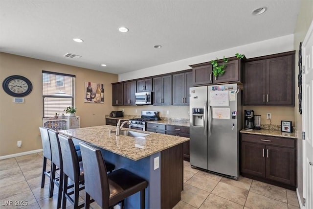 5309 Golden Melody Ln, North Las Vegas, NV 89081 - kitchen featuring appliances with stainless steel finishes, light tile patterned flooring, an island with sink, a kitchen bar, and light stone counters