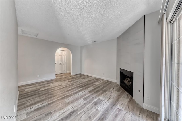 2200 S Fort Apache Rd Unit 2209, Las Vegas, NV 89117 - unfurnished living room featuring light wood-style flooring, a textured ceiling, a large fireplace, and arched walkways