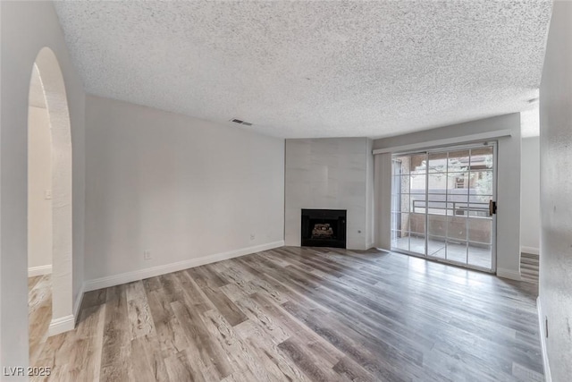 2200 S Fort Apache Rd Unit 2209, Las Vegas, NV 89117 - unfurnished living room featuring a textured ceiling, wood finished floors, a fireplace, and arched walkways
