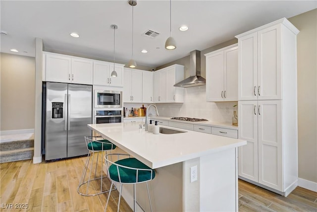 6591 Dove Point Pl, Las Vegas, NV 89130 - kitchen with appliances with stainless steel finishes, wall chimney range hood, light wood-style flooring, light countertops, and a kitchen island with sink