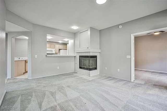 7400 W Flamingo Rd Unit 1051, Las Vegas, NV 89147 - unfurnished living room featuring light carpet, a tile fireplace, arched walkways, and a ceiling fan
