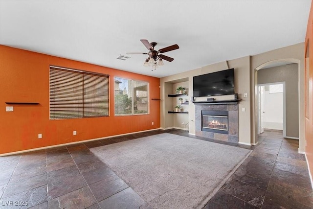 9413 Arcadia Woods Ct, Las Vegas, NV 89149 - unfurnished living room with built in shelves, stone tile flooring, ceiling fan, a fireplace, and arched walkways