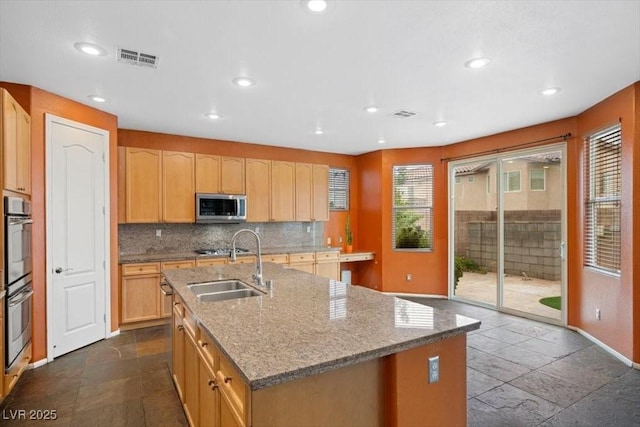 9413 Arcadia Woods Ct, Las Vegas, NV 89149 - kitchen featuring appliances with stainless steel finishes, decorative backsplash, light stone countertops, a center island with sink, and light brown cabinetry