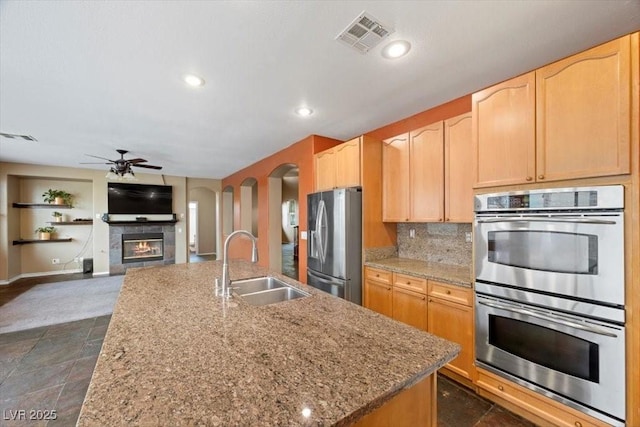 9413 Arcadia Woods Ct, Las Vegas, NV 89149 - kitchen with appliances with stainless steel finishes, a ceiling fan, a tile fireplace, recessed lighting, and an island with sink