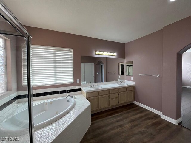 bathroom featuring double vanity, healthy amount of natural light, a tub with jets, and wood finished floors
