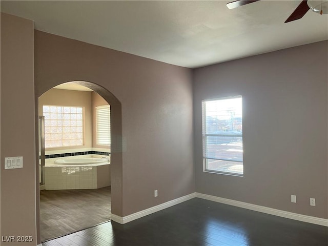 spare room with dark wood-style flooring, a ceiling fan, and arched walkways