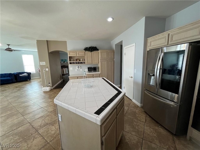 kitchen featuring appliances with stainless steel finishes, tile countertops, arched walkways, a center island, and ceiling fan