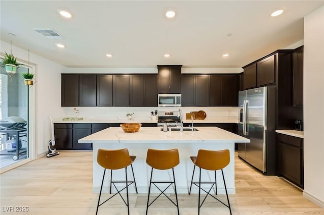 1289 Valencia Cliffs Ave, Henderson, NV 89012 - kitchen featuring stainless steel appliances, light wood-style floors, a breakfast bar, light stone counters, and recessed lighting