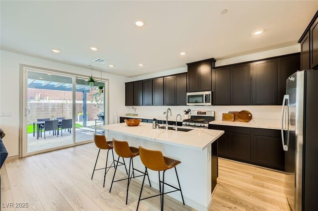 1289 Valencia Cliffs Ave, Henderson, NV 89012 - kitchen with appliances with stainless steel finishes, light wood-style flooring, a breakfast bar, a kitchen island with sink, and recessed lighting