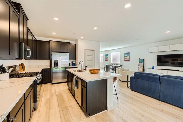 1289 Valencia Cliffs Ave, Henderson, NV 89012 - kitchen featuring stainless steel appliances, open floor plan, light stone countertops, light wood-type flooring, and a kitchen bar