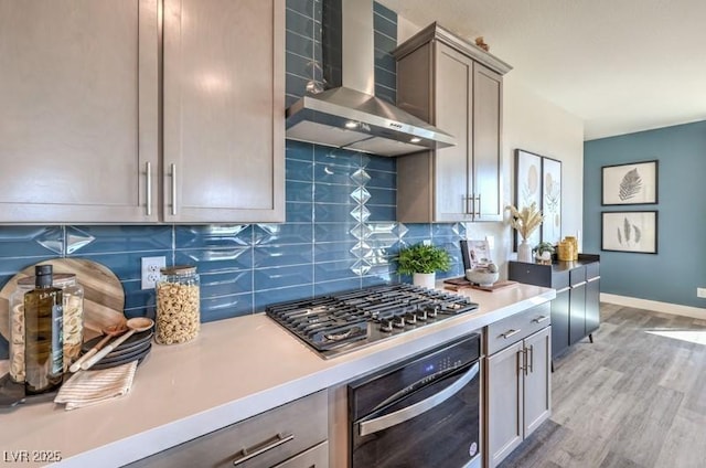 1408 Eva Creek Dr Unit 27, North Las Vegas, NV 89084 - kitchen with wall chimney exhaust hood, stainless steel appliances, decorative backsplash, light wood-type flooring, and light countertops