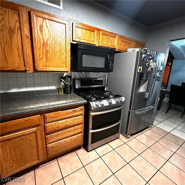 2709 Carroll St, North Las Vegas, NV 89030 - kitchen featuring appliances with stainless steel finishes, decorative backsplash, dark countertops, light tile patterned floors, and brown cabinets