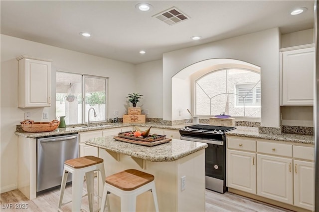 10921 Calcedonian St, Las Vegas, NV 89141 - kitchen with stainless steel appliances, light wood-type flooring, a center island, white cabinets, and light stone counters