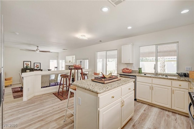 10921 Calcedonian St, Las Vegas, NV 89141 - kitchen with dishwasher, light wood-style floors, a kitchen island, white cabinets, and light stone countertops