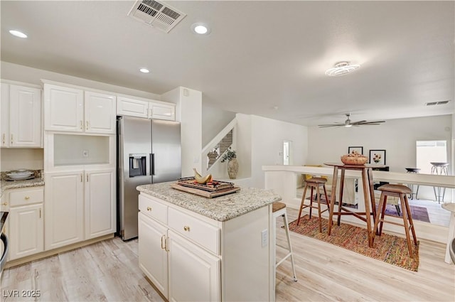 10921 Calcedonian St, Las Vegas, NV 89141 - kitchen with stainless steel fridge with ice dispenser, light wood-style floors, a center island, ceiling fan, and white cabinetry