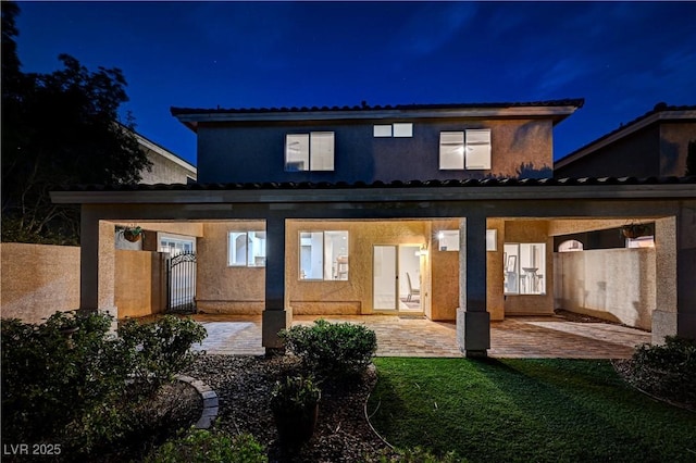 10921 Calcedonian St, Las Vegas, NV 89141 - back of house at twilight featuring a patio area, stucco siding, a gate, and a lawn