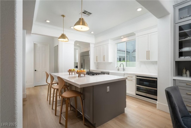11830 Kingsbarns Ct, Las Vegas, NV 89141 - kitchen with crown molding, appliances with stainless steel finishes, a kitchen bar, light wood-type flooring, and a kitchen island