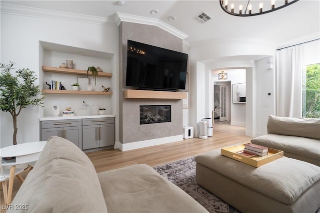 11830 Kingsbarns Ct, Las Vegas, NV 89141 - living room featuring light wood-type flooring, ornamental molding, a fireplace, arched walkways, and built in shelves