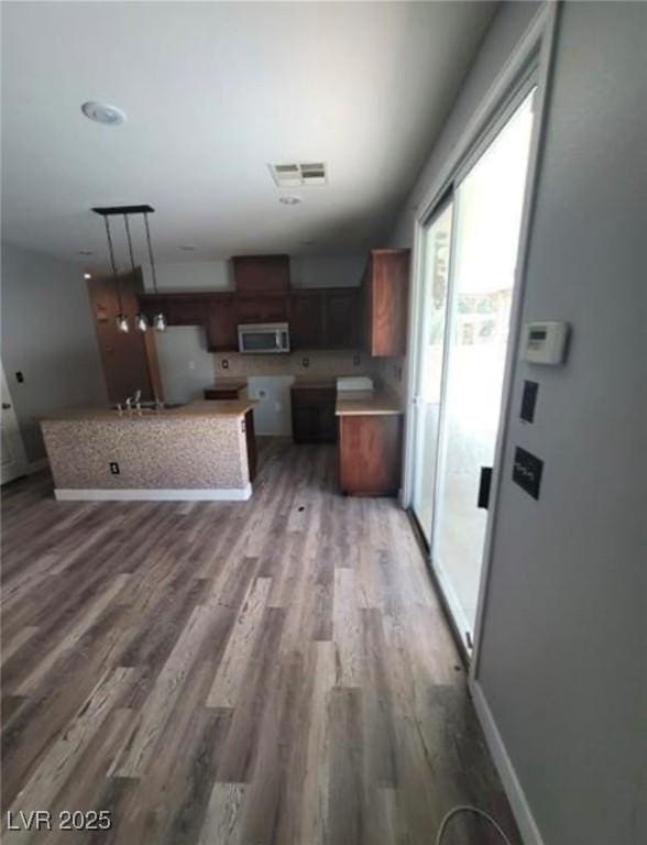 7349 Dolphine Crest Ave, Las Vegas, NV 89129 - kitchen with stainless steel microwave, wood finished floors, freestanding refrigerator, decorative light fixtures, and light countertops