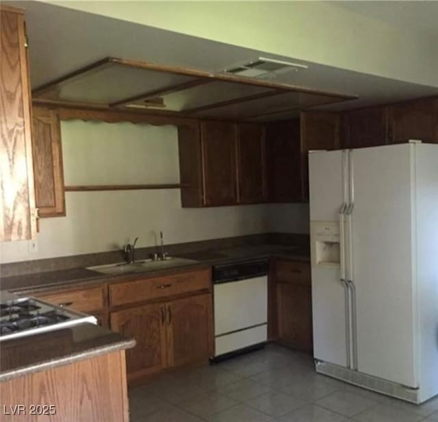 6671 W Tropicana Ave Unit 103, Las Vegas, NV 89103 - kitchen with white appliances, dark countertops, light tile patterned floors, and brown cabinetry