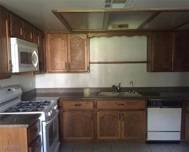 6671 W Tropicana Ave Unit 103, Las Vegas, NV 89103 - kitchen with white appliances, dark countertops, light tile patterned floors, and brown cabinets