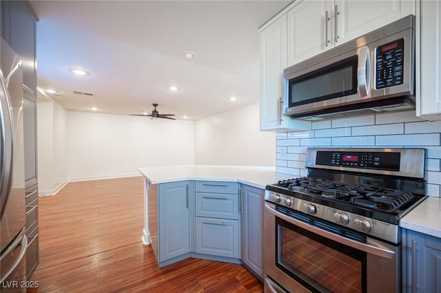 7388 Agonis St, Las Vegas, NV 89113 - kitchen featuring appliances with stainless steel finishes, light wood finished floors, tasteful backsplash, a peninsula, and light countertops