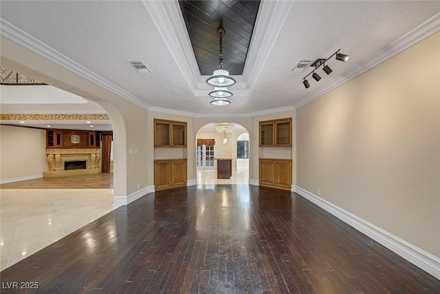 81 Quail Run Rd, Henderson, NV 89014 - unfurnished living room featuring a tray ceiling, arched walkways, wood-type flooring, a fireplace with raised hearth, and a chandelier
