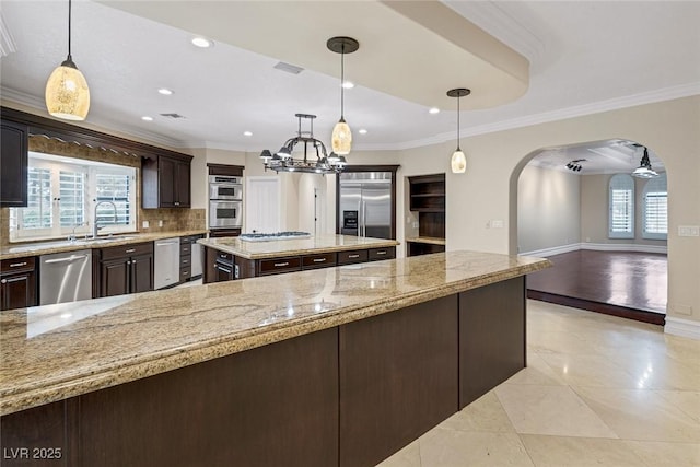 81 Quail Run Rd, Henderson, NV 89014 - kitchen featuring appliances with stainless steel finishes, arched walkways, dark brown cabinetry, a chandelier, and decorative backsplash