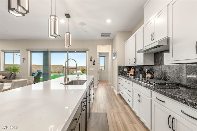 186 Vista Balla Ave, Las Vegas, NV 89138 - kitchen featuring under cabinet range hood, stainless steel gas stovetop, backsplash, dark stone countertops, and light wood-type flooring