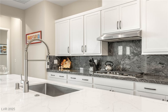 186 Vista Balla Ave, Las Vegas, NV 89138 - kitchen with stainless steel gas cooktop, under cabinet range hood, dark stone counters, and white cabinetry