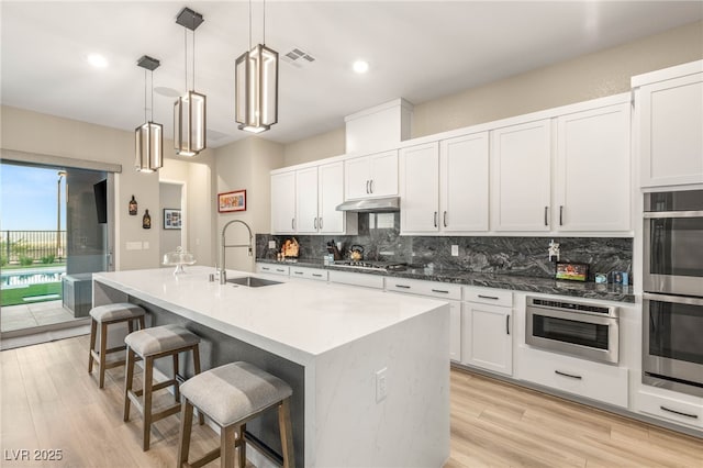 186 Vista Balla Ave, Las Vegas, NV 89138 - kitchen with stainless steel appliances, backsplash, under cabinet range hood, a breakfast bar, and light wood-type flooring